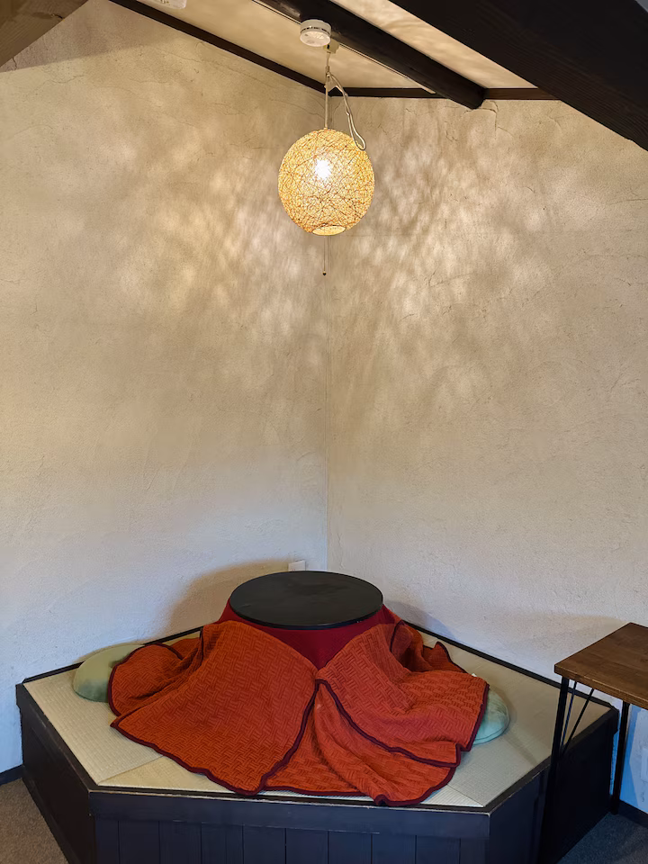 Aka room's tatami corner with a kotatsu under a woven pendant lamp