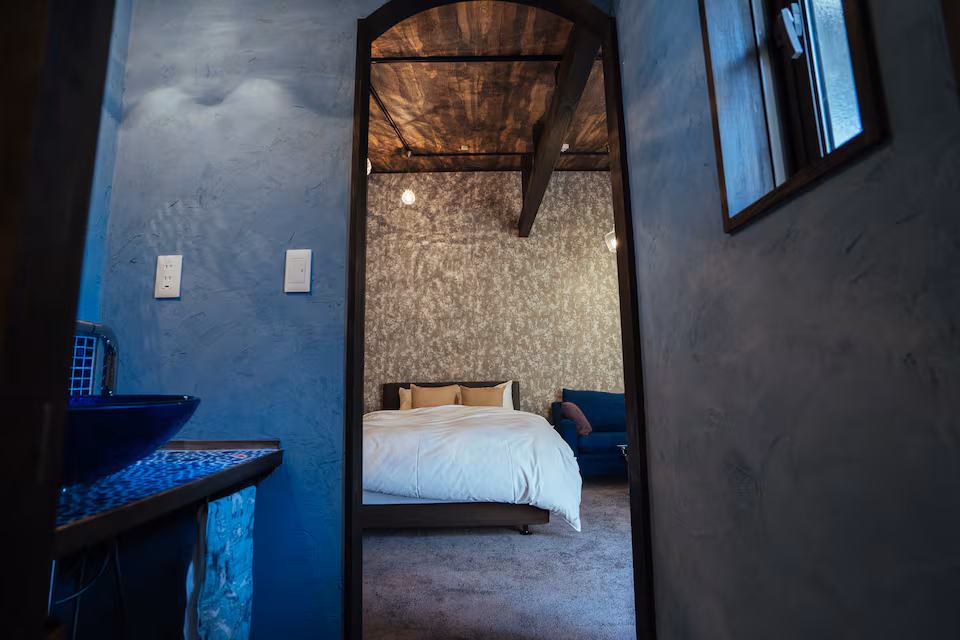 Akari cottage washbasin with a blue glass bowl, looking through an arched doorway to the bedroom