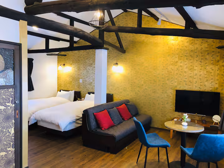 Fune cottage room under old beams, with beds, a sofa, a TV and a small round table
