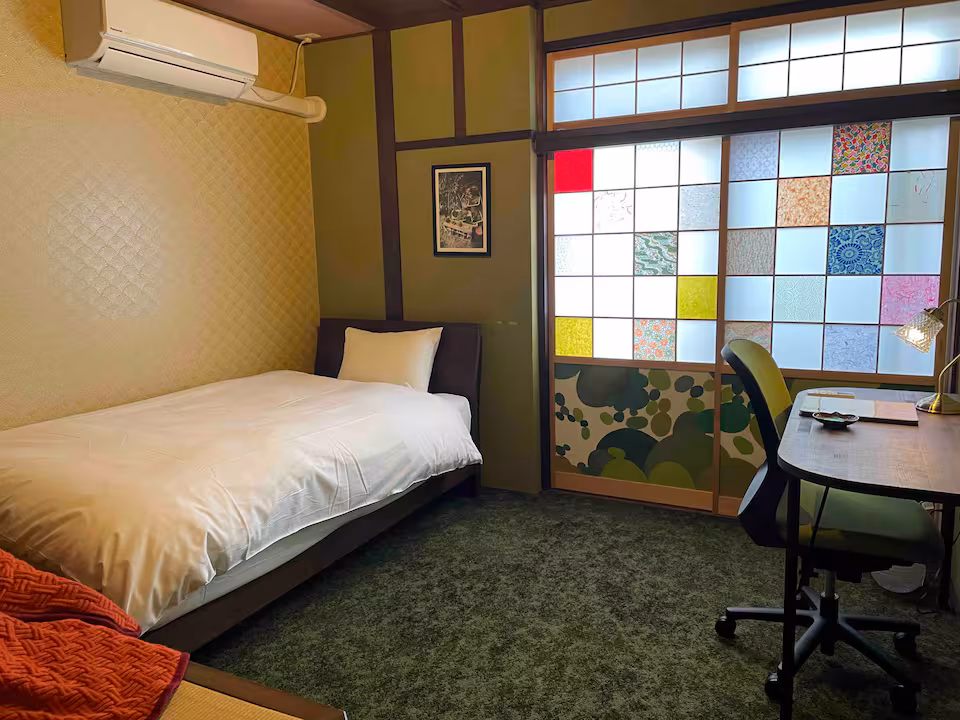 Koke room with a single bed, moss-green carpet, a desk and a coloured shoji window