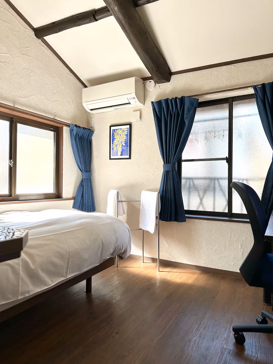 Kon room with a single bed, navy curtains and a desk chair by the window