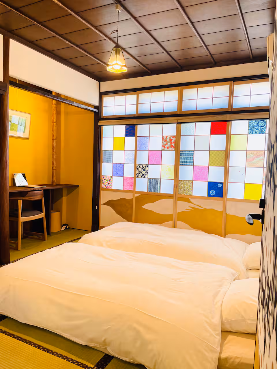 Shiro tatami room with two futons laid out, coloured paper shoji screens and a desk alcove
