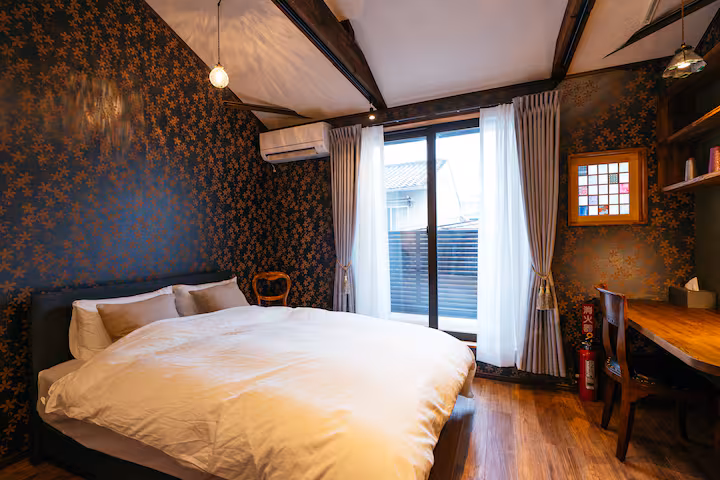 Tane cottage double bedroom with dark patterned wallpaper, a desk and a door to the balcony