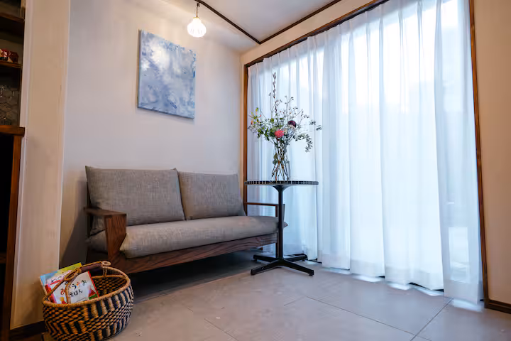 A sofa by tall windows with sheer curtains in Tane, a whole-house cottage in Nishijin
